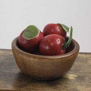 May include: Three red apples with green leaves in a wooden bowl. The bowl is brown and has a natural wood grain.