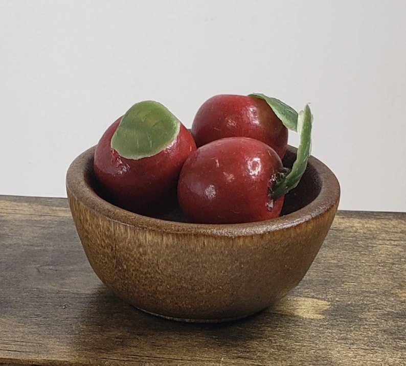 May include: Three red apples with green leaves in a wooden bowl. The bowl is brown and has a natural wood grain.