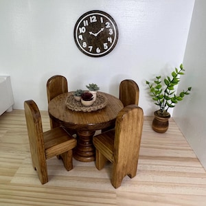 May include: Miniature wooden dining set with a round table and four chairs. The table is topped with a woven placemat and small potted succulents. A dark brown clock hangs on the wall above the table.
