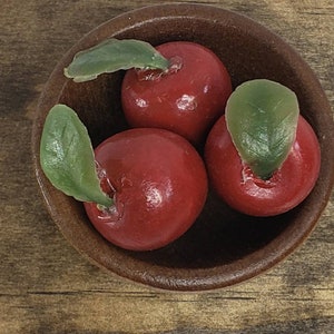 May include: Three red apples with green leaves in a brown wooden bowl. The apples are shiny and smooth.