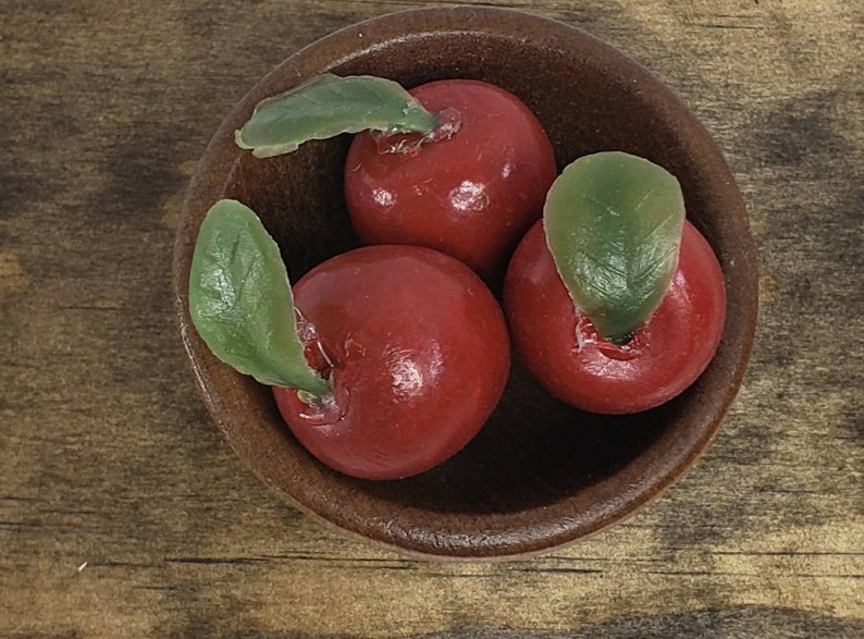May include: Three red apples with green leaves in a brown wooden bowl. The apples are shiny and smooth.