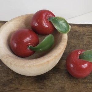 May include: Three red apples with green leaves in a small wooden bowl. The bowl is sitting on a wooden surface.