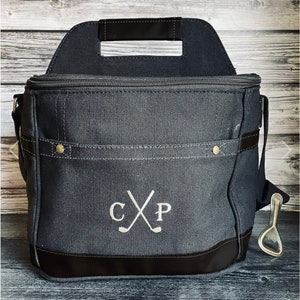 May include: A black canvas cooler bag with a zippered top, a handle, and a shoulder strap. The bag has a bottle opener attached to the strap. The bag has a monogram with the initials "CXP" and two crossed golf clubs.