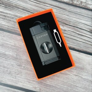 May include: A black cigar cutter with the word "CARTER" printed on it, in an orange box with a small silver tool.