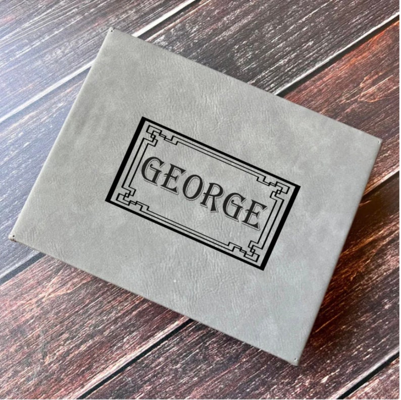 May include: A gray, rectangular box with a black border and the name "GEORGE" inscribed in the center.