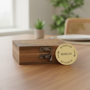 May include: A rectangular dark brown wooden box with a metal latch and the text "HANDLE CRITICAL CHOICES HERE" engraved on the lid. Beside the box sits a round gold-colored metal coin featuring the text "DECISION COIN", "REBECCA", and "FLIP TO DECIDE".
