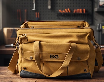 May include: A mustard yellow canvas tool bag featuring a wide zippered opening, two sturdy fabric handles, and a front pocket with the letters BG embroidered in black. The base is reinforced with a dark gray material and includes metal hardware.
