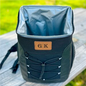 Pode incluir: Mochila t&eacute;rmica preta com um remendo de couro marrom que diz "G|K". A mochila tem um fecho de cord&atilde;o e um bolso com z&iacute;per.