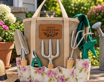 May include: A tan canvas gardening tote bag with a floral print base and a leather patch reading "MOM'S GARDENING TOOLS". The bag contains a metal trowel, a three-pronged hand cultivator, a green hand pruner, and a green plastic spray bottle.