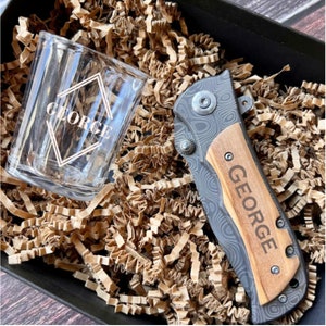 May include: A personalized gift set with a small glass shot glass and a pocket knife. The shot glass and knife are both engraved with the name "GEORGE".