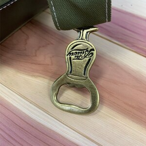 May include: A gold-colored bottle opener with a black inscription that reads "Tommy's NYC".