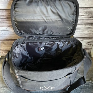 May include: Black canvas bag with a brown leather trim and a zipper closure. The bag has a large main compartment and a smaller pocket on the front. The bag is monogrammed with the initials "CXP".