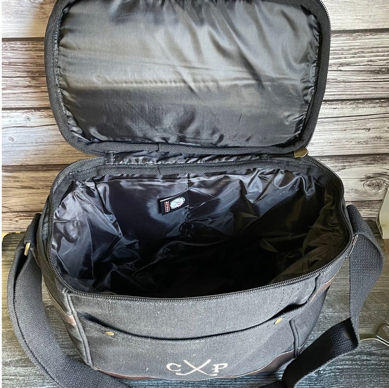 May include: Black canvas bag with a brown leather trim and a zipper closure. The bag has a large main compartment and a smaller pocket on the front. The bag is monogrammed with the initials "CXP".
