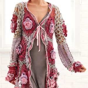 May include: A crocheted cardigan with a floral design in shades of pink, grey, and burgundy. The cardigan has a tie closure at the neckline and features a delicate openwork pattern.