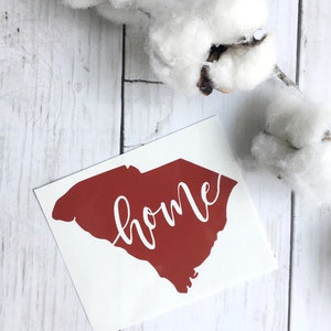 May include: A red vinyl decal of the state of South Carolina with the word "home" written in white cursive lettering.