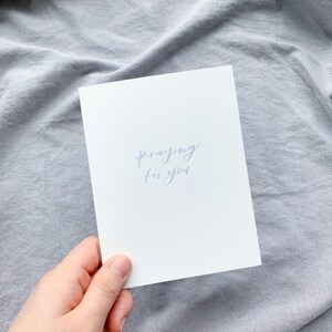 May include: A white card with the words "praying for you" written in blue ink.