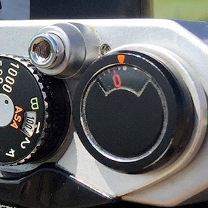 May include: Close-up of a silver camera with a black dial that has numbers from 8 to 1000. The dial is labeled "ASA". There is a black dial with a needle that reads "0".