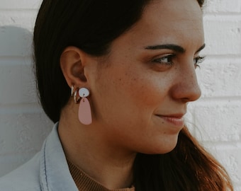 May include: A woman with long brown hair wearing a light blue denim jacket over a brown and white striped sweater. She is wearing a pair of pink and white dangle earrings.