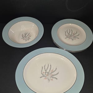 May include: A set of vintage dinnerware featuring a blue rim with a white center and a delicate floral design. The set includes a large dinner plate, a smaller salad plate, and a soup bowl.