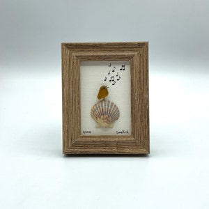 May include: A framed artwork featuring a small yellow glass bird perched on a seashell with musical notes drawn around it. The artwork is titled "Songbird" and signed "LY 2021".