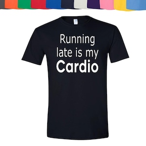 Może przedstawiać: Czarna koszulka z białym napisem "Running late is my Cardio". Różne inne kolorowe koszulki są wyświetlane nad główną koszulką. Koszulka ma krótkie rękawy.