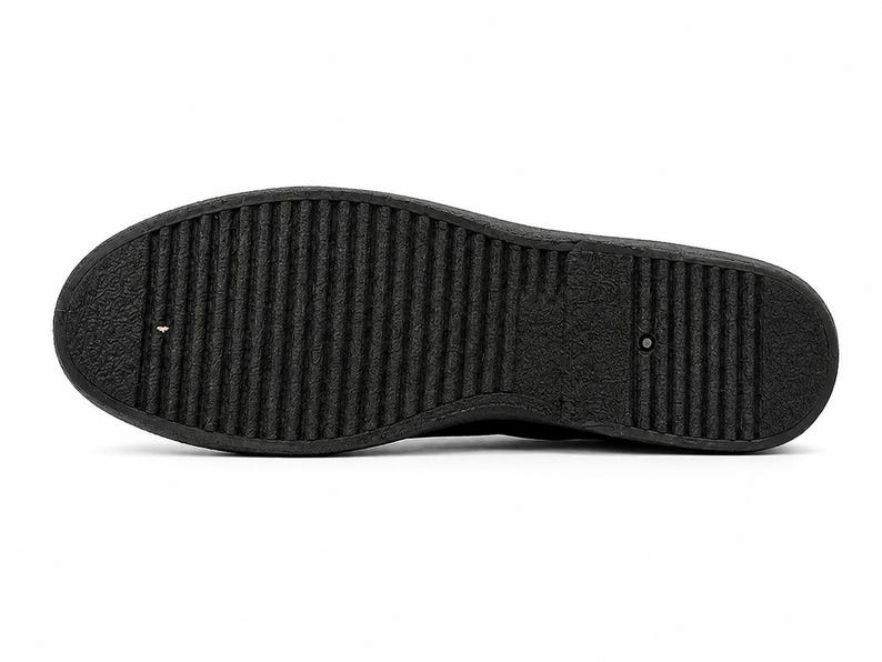 May include: A close-up of the sole of a black shoe. The sole is made of a textured, ridged material. The shoe is on a white background.