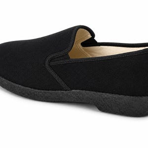 May include: Black slip-on shoe with a rounded toe and a low, textured sole. The shoe features a simple design with a canvas upper and a contrasting, darker sole. The interior lining is a light beige color.