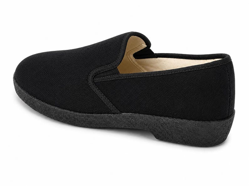 May include: Black slip-on shoe with a rounded toe and a low, textured sole. The shoe features a simple design with a canvas upper and a contrasting, darker sole. The interior lining is a light beige color.
