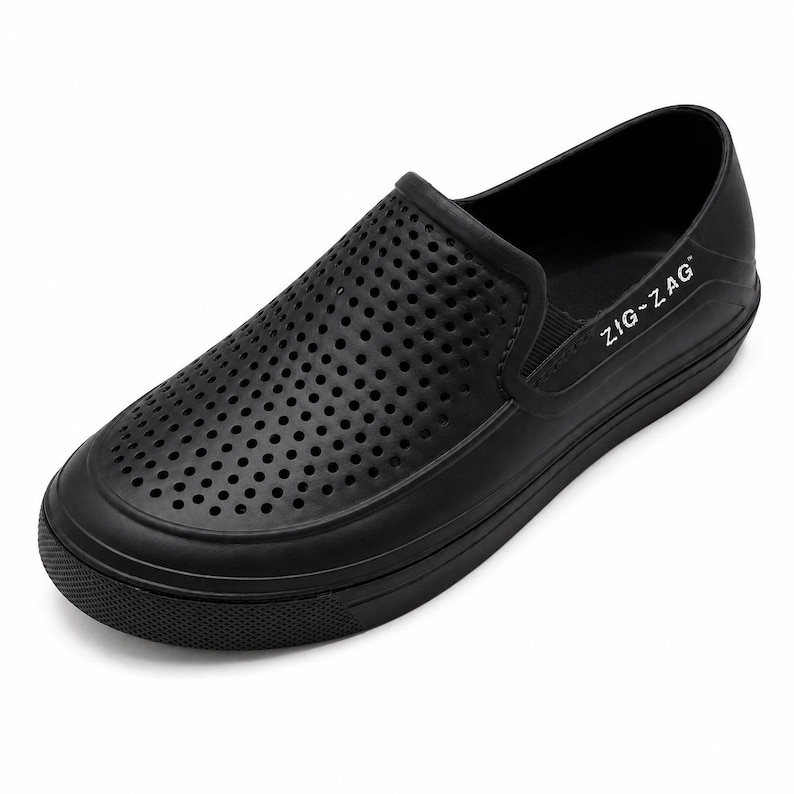 May include: Black slip-on shoe with a perforated upper for breathability. The shoe features a rounded toe, a thick sole, and the text "ZIG-ZAG" on the side. This casual shoe is designed for comfort and everyday wear.