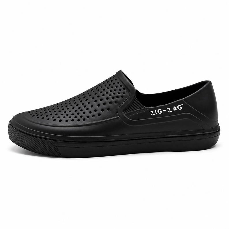 May include: Black slip-on shoe with a perforated upper and a thick sole. The shoe features the text "ZIG-ZAG" in white on the side. The design is simple and modern, suitable for casual wear.