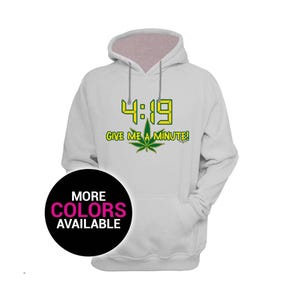 May include: White hoodie with a drawstring and a front pocket. The front features the text "4:19 GIVE ME A MINUTE!" in yellow and green, along with a cannabis leaf graphic. A black circle with "MORE COLORS AVAILABLE" is in the lower left.
