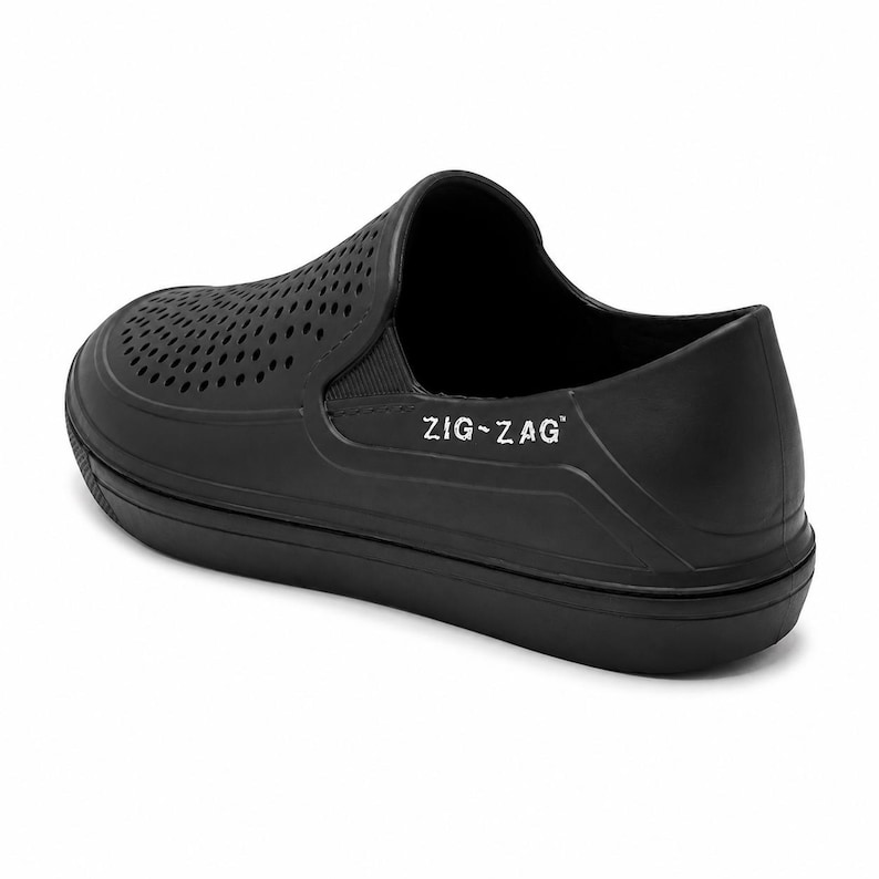 May include: Black slip-on shoe with a perforated upper and a thick sole. The shoe features the text "ZIG-ZAG" in white on the side. The shoe is made of a solid, matte material.