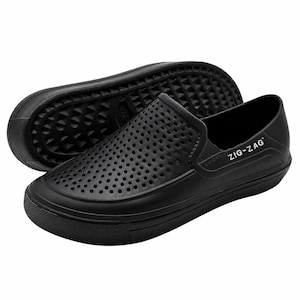May include: Black slip-on shoes with a perforated upper design. The shoes have a rounded toe and a thick, textured sole. The brand name "ZIG-ZAG" is printed on the side of the shoe. One shoe is positioned on top of the other.