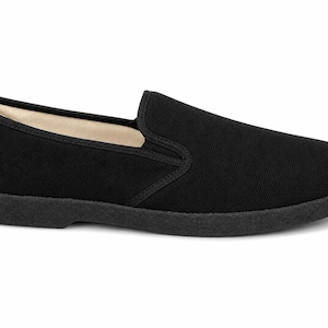 May include: A single black slip-on shoe. The shoe features a solid black canvas upper with a rounded toe and a low-profile, black rubber sole. The interior lining is a light beige color.