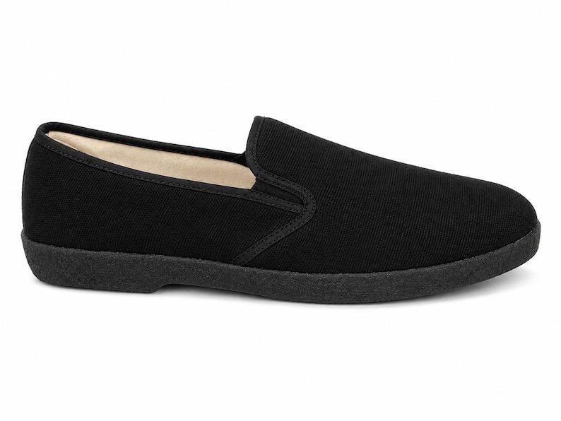 May include: A single black slip-on shoe. The shoe features a solid black canvas upper with a rounded toe and a low-profile, black rubber sole. The interior lining is a light beige color.