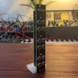 Könnte beinhalten: Ein schwarzes Minx Eurorack-Modul mit mehreren Buchsen für Audio- und CV-Verbindungen. Das Modul ist auf einer Holzoberfläche montiert.
