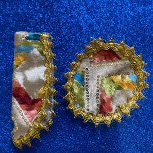 May include: Two decorative, embroidered coasters and a napkin. The items feature a cream-colored background with colorful, abstract patterns in red, green, yellow, and blue. Gold trim and sequins outline the edges, adding a touch of elegance.