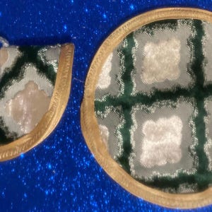 May include: Two decorative items with a gold trim. One is a round coaster with a green and cream checkered pattern. The other is a matching bookmark with a green and white tassel. Both items have a gold trim.