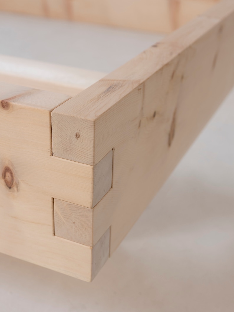 K&ouml;nnte beinhalten: Nahaufnahme einer Holzeckverbindung, die die komplizierte Schwalbenschwanzkonstruktion zeigt. Das Holz ist hellbraun und hat eine nat&uuml;rliche Maserung.