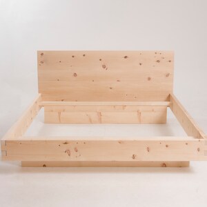 K&ouml;nnte beinhalten: Ein Holzbettgestell mit einem Kopfteil und einem Lattenrost. Der Rahmen ist aus Naturholz mit einer hellbraunen Oberfl&auml;che.