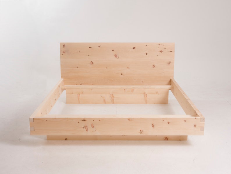 K&ouml;nnte beinhalten: Ein Holzbettgestell mit einem Kopfteil und einem Lattenrost. Der Rahmen ist aus Naturholz mit einer hellbraunen Oberfl&auml;che.