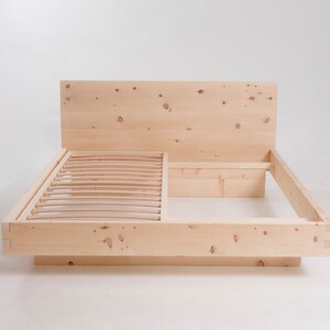 K&ouml;nnte beinhalten: Ein Holzbettgestell mit einem Lattenrost-Kopfteil und einem Lattenrost-Fu&szlig;teil. Der Rahmen ist aus Naturholz mit einer hellbraunen Oberfl&auml;che.