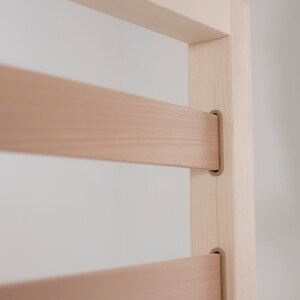 K&ouml;nnte beinhalten: Nahaufnahme eines Holzrahmens mit horizontalen Latten. Der Rahmen ist aus hellem Holz und hat eine nat&uuml;rliche Oberfl&auml;che. Die Latten werden durch Metallwinkel gehalten.