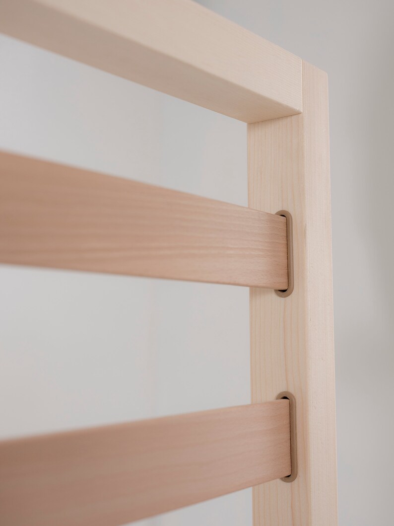 K&ouml;nnte beinhalten: Nahaufnahme eines Holzrahmens mit horizontalen Latten. Der Rahmen ist aus hellem Holz und hat eine nat&uuml;rliche Oberfl&auml;che. Die Latten werden durch Metallwinkel gehalten.