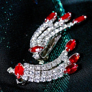 May include: Two silver hair clips with red rhinestone accents. The clips are decorated with rows of clear rhinestones.
