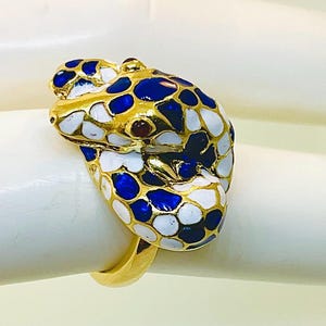 May include: A gold-toned ring featuring a snake design. The snake's head is adorned with blue, white, and gold enamel, with small red accents. The ring is a unique piece of jewelry.