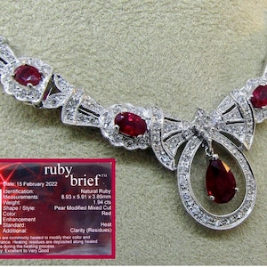 Può includere: Elegante collana in argento con design a fiocco, con più rubini ovali e un pendente a forma di pera. La collana è adornata con piccoli diamanti scintillanti. È visibile anche la scheda informativa del rubino.