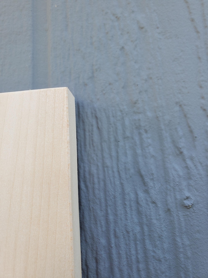 May include: A rectangular piece of light-colored, smooth-grained wood board with a clean, straight edge. The wood features a natural, pale beige tone with subtle grain patterns visible across its flat surface and a sharp, defined corner.