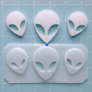 May include: A clear silicone mold with six alien head shapes. The mold is on a blue grid background. The text "Magical Molds" is visible in the image.