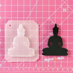May include: A clear plastic mold for making resin crafts. The mold is shaped like a seated Buddha figure. The mold is on a pink cutting mat with a ruler.